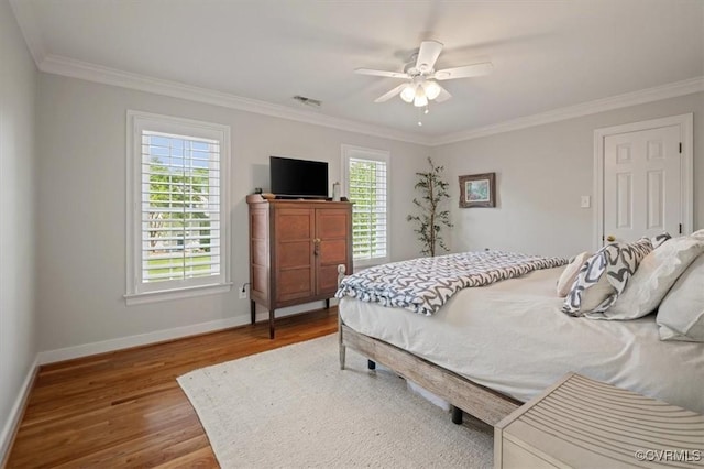 bedroom featuring wood finished floors, ornamental molding, visible vents, a ceiling fan, and baseboards