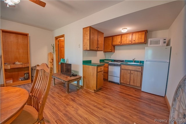 kitchen featuring wood finished floors, white appliances, brown cabinets, a sink, and a ceiling fan