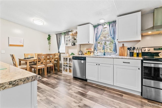 kitchen featuring a sink, light wood-type flooring, wall chimney exhaust hood, white cabinets, and appliances with stainless steel finishes