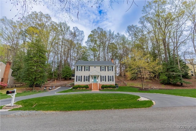 colonial inspired home featuring curved driveway, a chimney, and a front yard