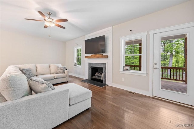living room with a ceiling fan, visible vents, a fireplace with raised hearth, and dark wood-type flooring