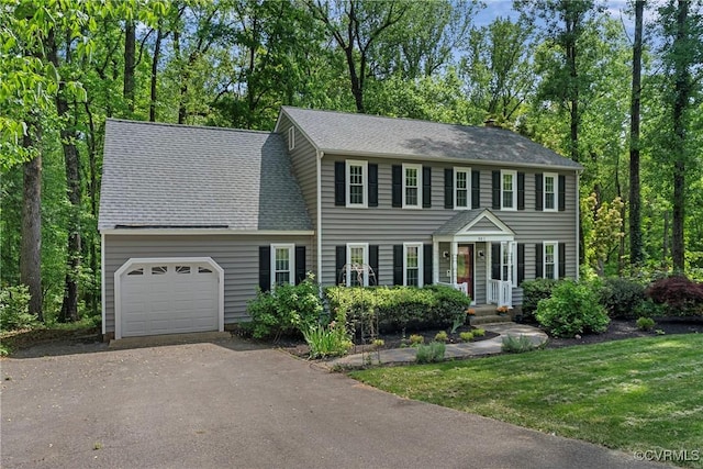 colonial house featuring an attached garage, a shingled roof, aphalt driveway, and a front yard