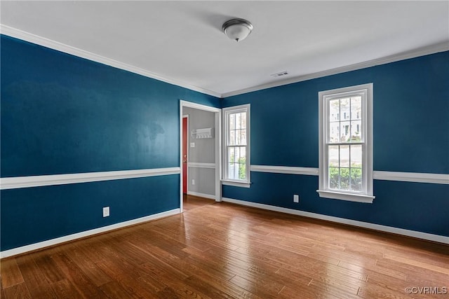spare room featuring baseboards, ornamental molding, wood finished floors, and visible vents
