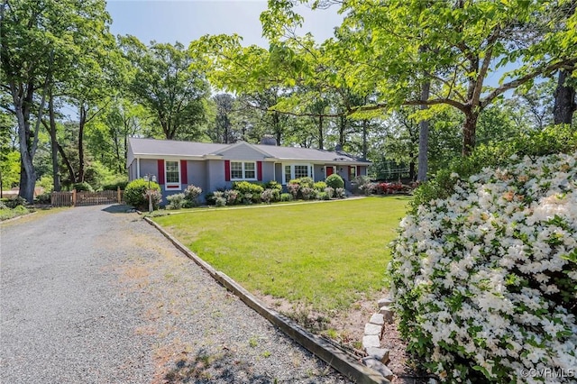ranch-style home featuring fence, a front yard, and gravel driveway