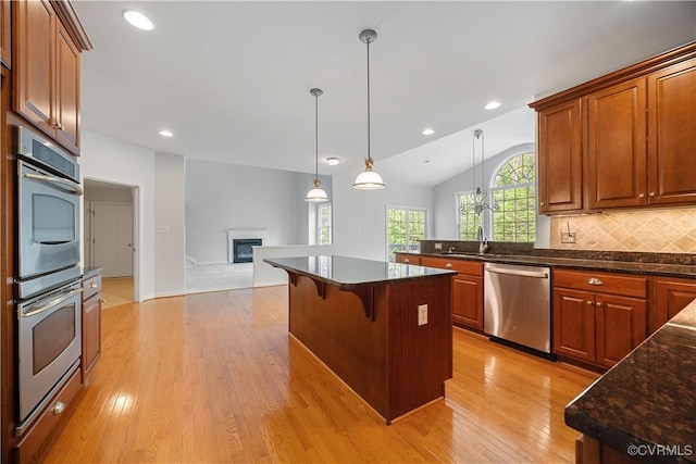 kitchen featuring a kitchen breakfast bar, appliances with stainless steel finishes, light wood-style floors, open floor plan, and a glass covered fireplace