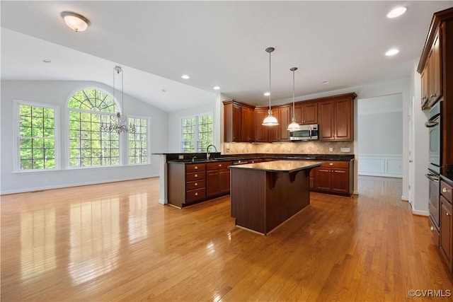 kitchen featuring lofted ceiling, stainless steel microwave, dark countertops, light wood-style floors, and a center island
