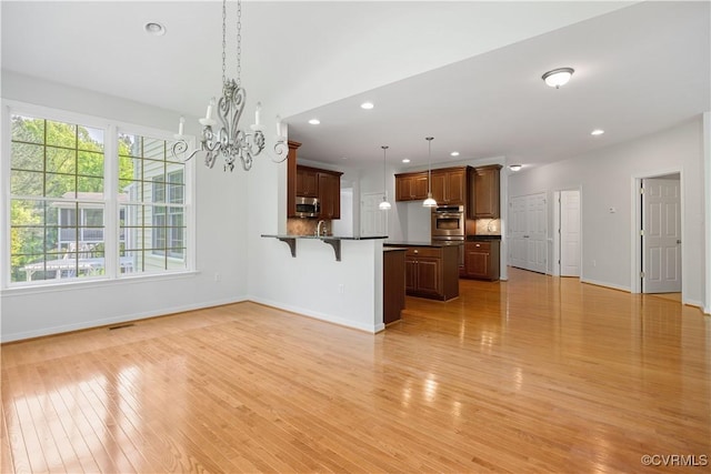 interior space featuring an inviting chandelier, light wood-style flooring, stainless steel appliances, dark countertops, and a kitchen bar