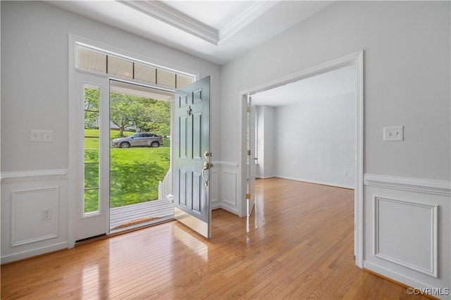 doorway to outside with ornamental molding, a wainscoted wall, light wood-style floors, and a decorative wall