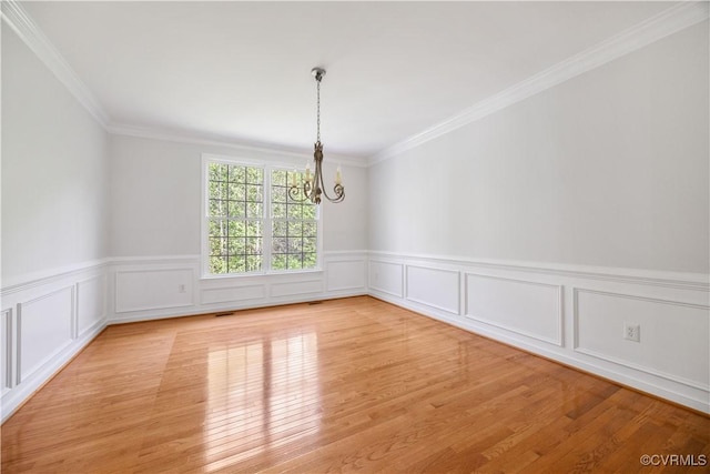 unfurnished dining area featuring crown molding, a wainscoted wall, a chandelier, and light wood-style floors