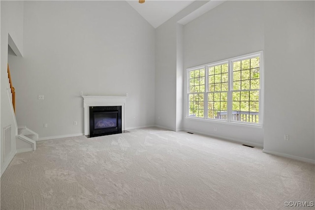 unfurnished living room with visible vents, high vaulted ceiling, a fireplace with flush hearth, and carpet flooring