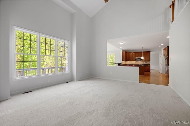 unfurnished living room with recessed lighting, a high ceiling, visible vents, light carpet, and baseboards