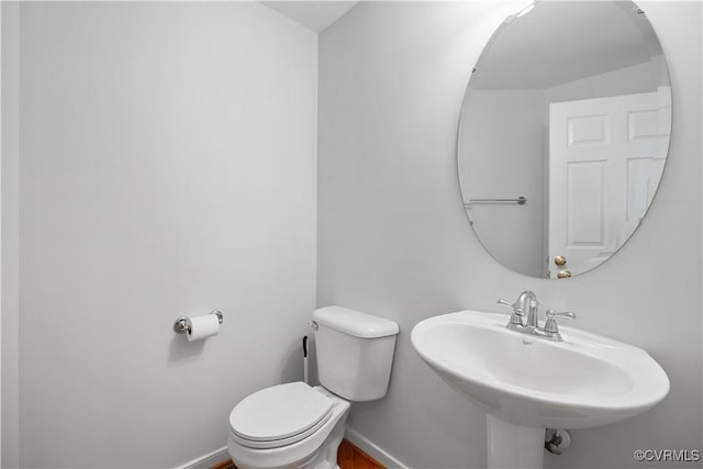 half bathroom with toilet, a sink, and baseboards