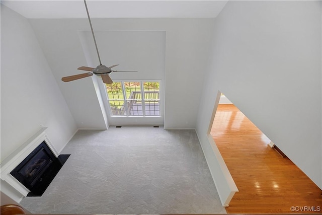 unfurnished living room with carpet, ceiling fan, baseboards, a fireplace, and a towering ceiling