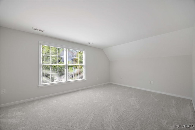additional living space featuring visible vents, light carpet, vaulted ceiling, and baseboards
