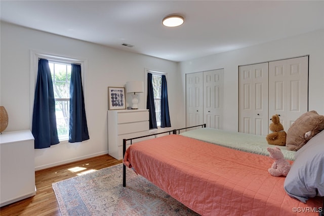 bedroom with wood finished floors, baseboards, and two closets