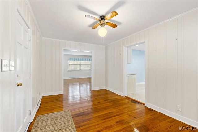 empty room with crown molding, a ceiling fan, hardwood / wood-style floors, and baseboards