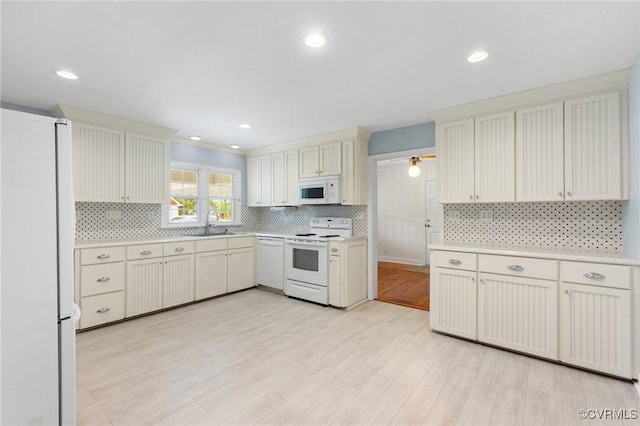 kitchen with backsplash, white appliances, light countertops, and a sink