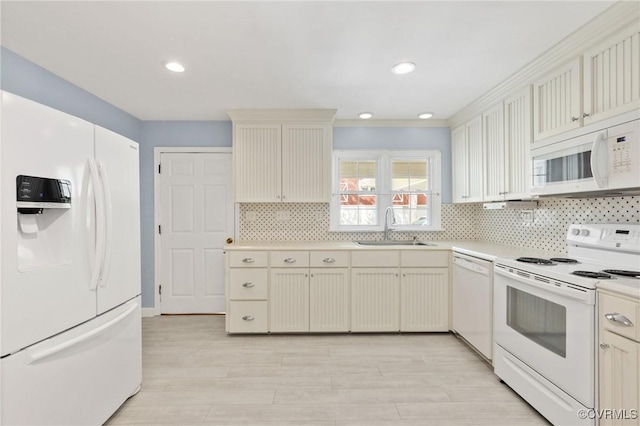 kitchen with light wood finished floors, a sink, white appliances, tasteful backsplash, and light countertops