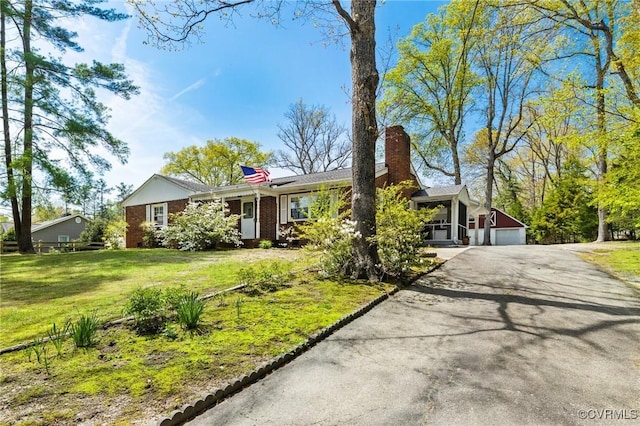 single story home featuring a front lawn, a garage, a chimney, driveway, and brick siding