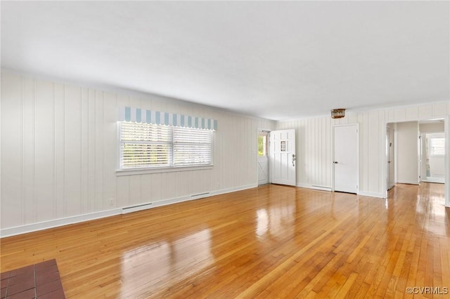 unfurnished living room with a baseboard radiator, a wealth of natural light, light wood finished floors, and baseboards