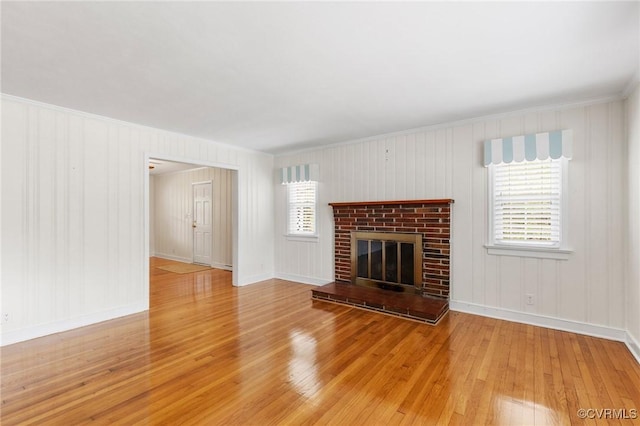unfurnished living room featuring crown molding, hardwood / wood-style floors, a brick fireplace, and baseboards