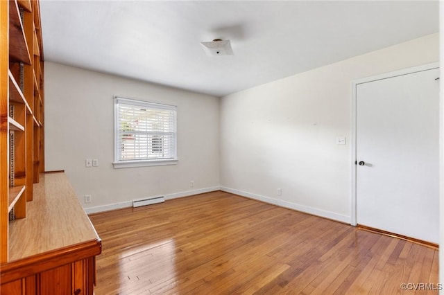 spare room featuring baseboards, a baseboard heating unit, and wood-type flooring