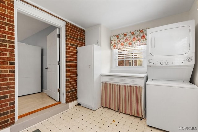 washroom featuring light floors, brick wall, and stacked washing maching and dryer