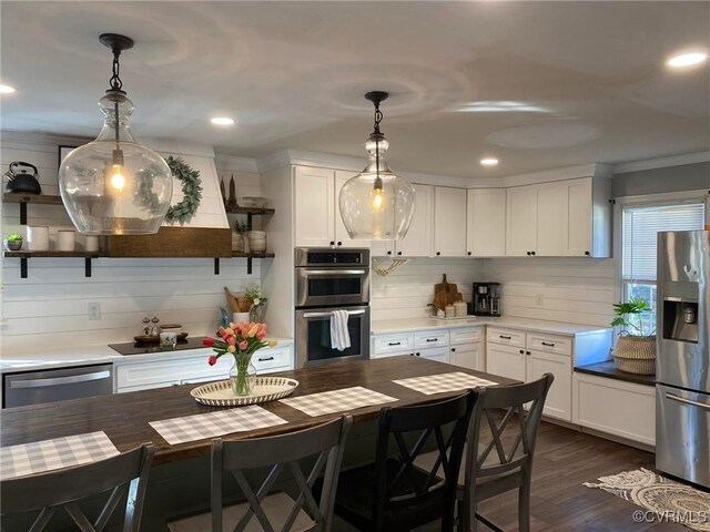 kitchen with ornamental molding, dark wood-type flooring, white cabinets, appliances with stainless steel finishes, and decorative light fixtures