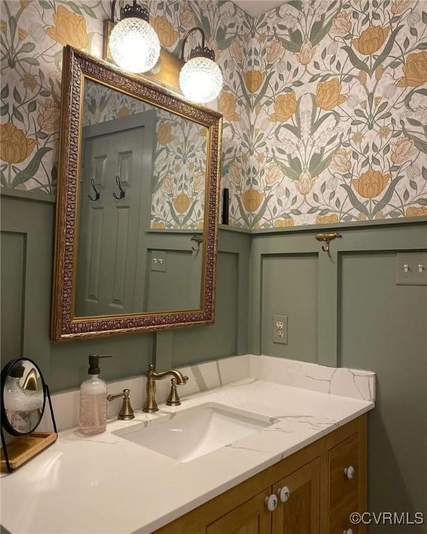 bathroom featuring vanity, a decorative wall, and wallpapered walls