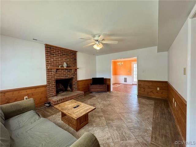 living room with visible vents, ceiling fan with notable chandelier, a wainscoted wall, and wooden walls