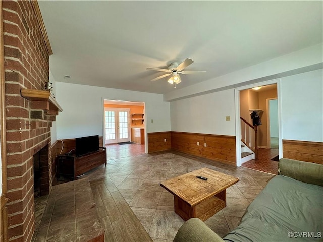living room with ceiling fan, french doors, wainscoting, wood walls, and stairs