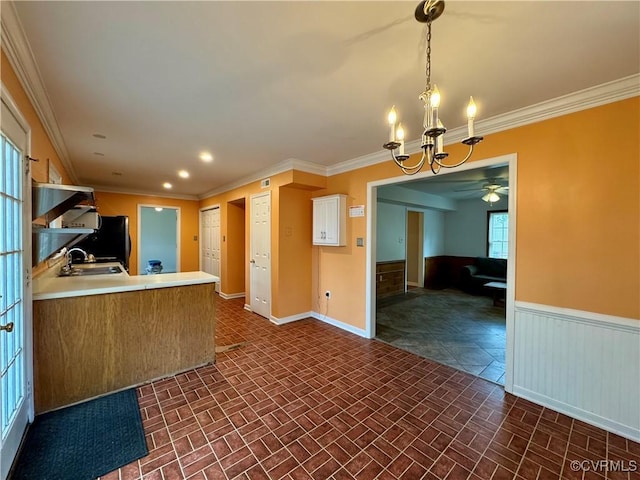 kitchen with crown molding, brick patterned floor, a sink, and ceiling fan with notable chandelier