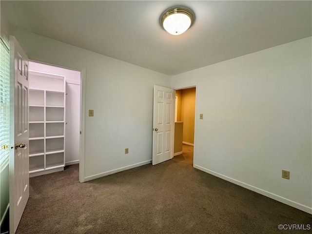 unfurnished bedroom featuring baseboards, a walk in closet, dark carpet, and a closet