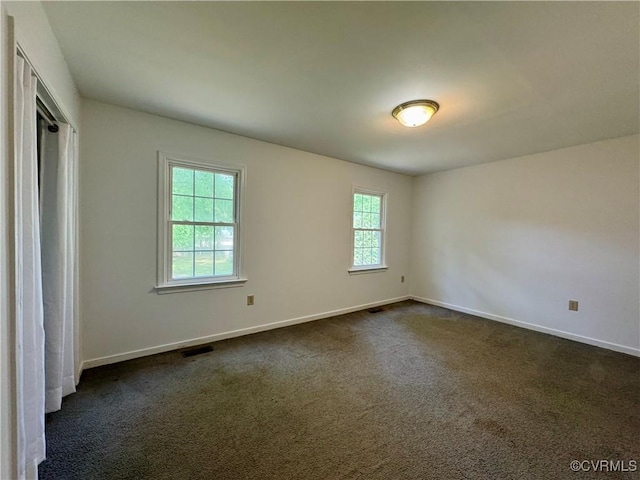 unfurnished room with dark carpet, baseboards, and visible vents