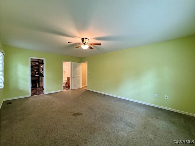 unfurnished bedroom featuring dark colored carpet, baseboards, a walk in closet, and ensuite bath