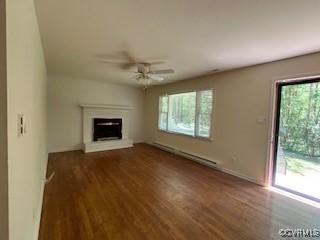 unfurnished living room featuring wood finished floors, ceiling fan, a fireplace with raised hearth, and a baseboard heating unit