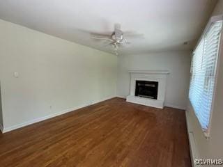 unfurnished living room featuring ceiling fan, baseboards, wood finished floors, and a glass covered fireplace