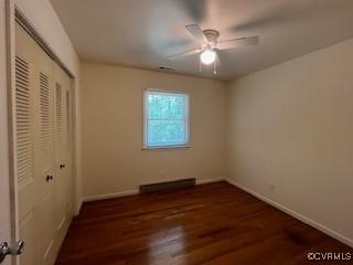 unfurnished bedroom with wood finished floors, a baseboard heating unit, a closet, baseboards, and a ceiling fan