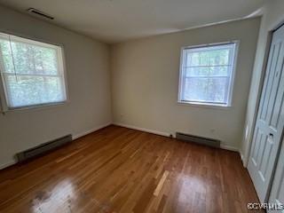 unfurnished bedroom featuring multiple windows, baseboard heating, wood finished floors, and a baseboard radiator