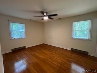 empty room with baseboards, wood finished floors, a baseboard heating unit, and ceiling fan