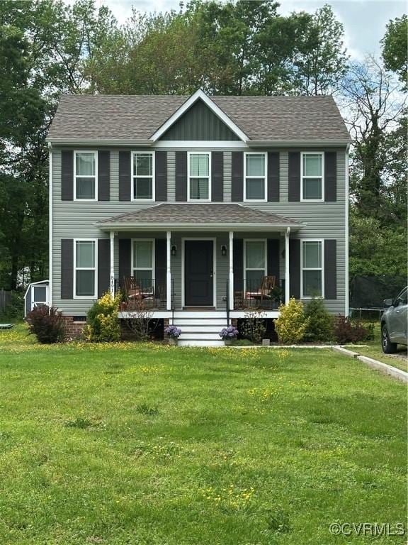 colonial inspired home with roof with shingles, covered porch, and a front yard