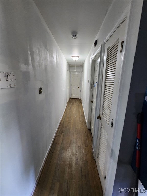 hallway featuring baseboards, attic access, and dark wood-type flooring