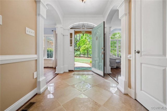 foyer entrance with baseboards, arched walkways, decorative columns, and crown molding