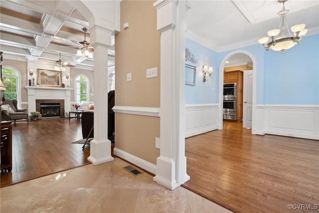 interior space featuring visible vents, decorative columns, wood finished floors, a fireplace, and ceiling fan with notable chandelier