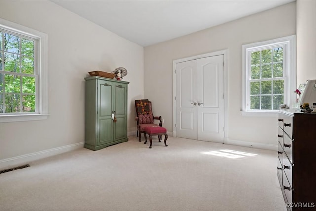 living area with visible vents, a wealth of natural light, and light colored carpet