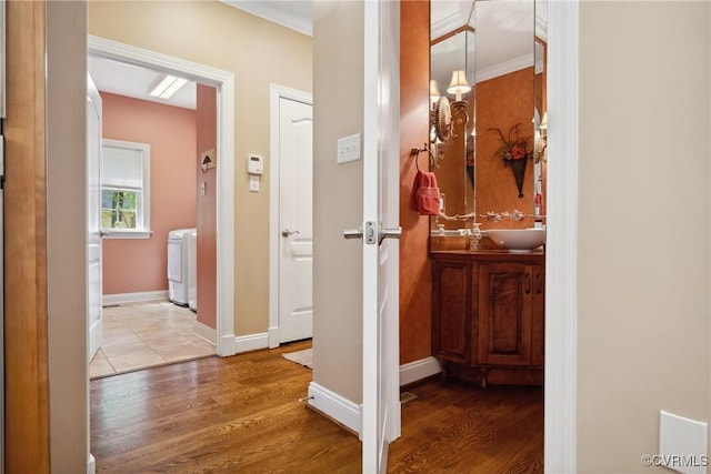 hall with washer / dryer, baseboards, ornamental molding, and wood finished floors