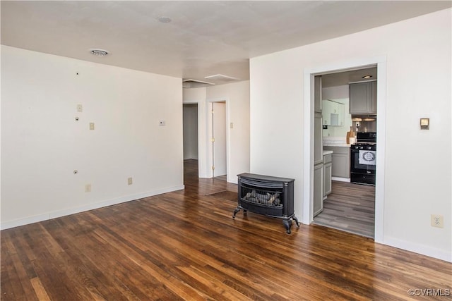 unfurnished room featuring baseboards, wood finished floors, and a wood stove