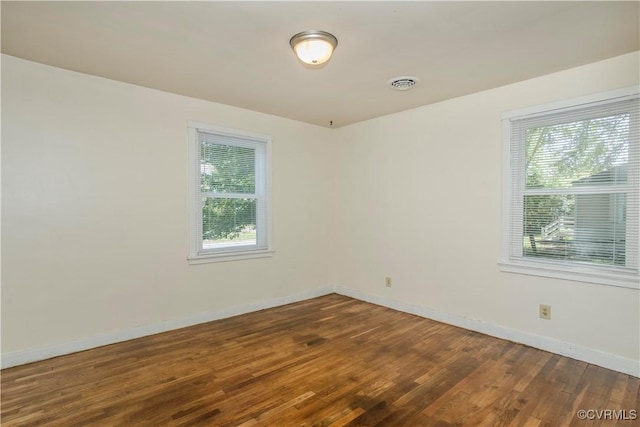empty room featuring baseboards, wood finished floors, and visible vents