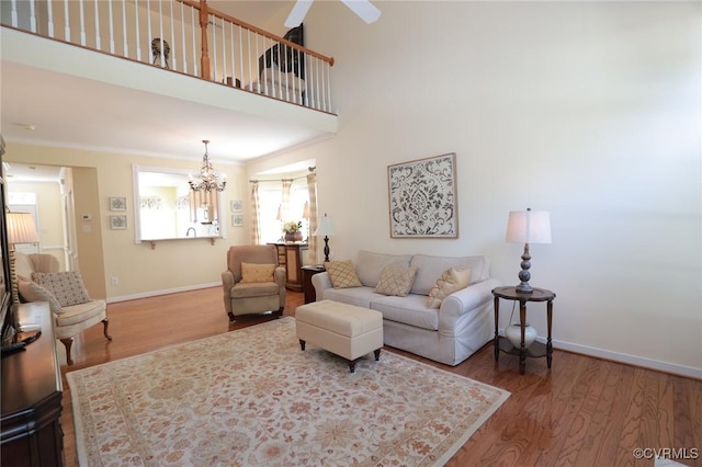 living room featuring baseboards, ornamental molding, wood finished floors, and ceiling fan with notable chandelier