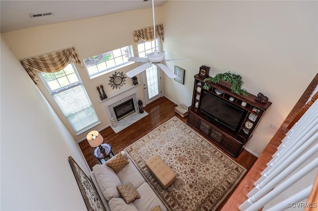 living area featuring ceiling fan, a premium fireplace, wood finished floors, and a towering ceiling